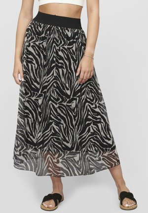 Maxikleid mit Zebra-Muster in Schwarz und Creme, mit schwarzem elastischem Bund und transparenter Textur, kombiniert mit schwarzen Slipper-Sandalen.