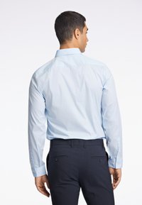 Camicia azzurra a maniche lunghe con colletto a punta, polsini con bottoni e texture morbida, abbinata a pantaloni scuri con tasche posteriori con bottoni.