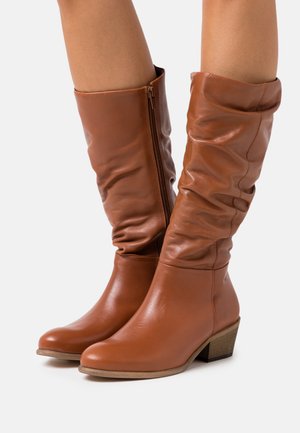 Brown leather knee-high boots with a slouchy design, side zipper, and a low stacked heel, featuring smooth texture and a sleek silhouette.