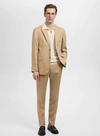 Traje de color beige claro, corte entallado con un ligero brillo, chaqueta de un solo botón, pantalones a juego, usado sobre una camiseta polo crema, zapatos de cuero.
