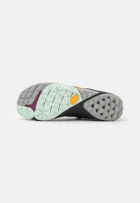 Suela de zapatilla deportiva en negro y gris con goma texturizada verde menta, acentos en púrpura y una mezcla de patrones de banda de rodadura triangulares y hexagonales.
