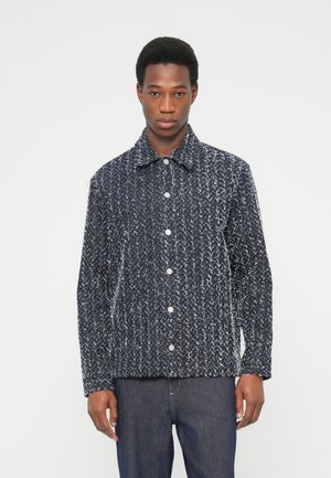 Giacca intrecciata blu navy e bianca con collo a camicia, chiusura con bottoni e maniche lunghe. Tessuto strutturato con un motivo astratto sottile.