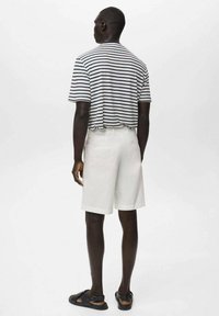 Randig kortärmad skjorta i svart och vitt, matchad med vita shorts. Modellen bär svarta sandaler. Enkel, avslappnad design med en lös passform.