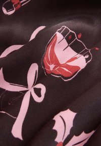 Tissu sombre avec des motifs floraux rouges et roses, comprenant des nœuds et des dessins abstraits. Texture lisse avec une légère brillance.