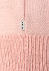 Helles rosa Strickpullover mit gerippter Textur am Saum, versehen mit einem kleinen gewebten Etikett, das den Markennamen "Maerz" zeigt.