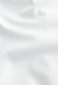 Weißer Baumwollstoff mit einer glatten Textur und feinem diagonalen Gewebemuster, der weiche Falten und eine natürliche Drapierung zeigt.