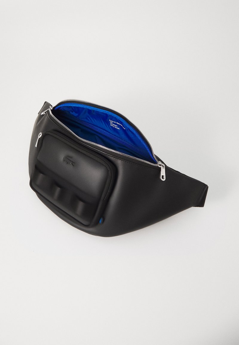 Sacoche noire avec une finition mate, dotée d'une poche avant texturée et d'un intérieur bleu vif. Fermeture à glissière et bandoulière réglable.