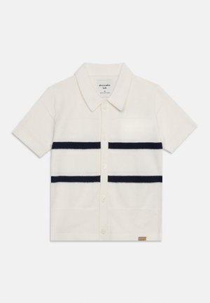 Chemise blanche en maille à manches courtes avec col, boutonnage devant et deux paires de rayures noires horizontales sur la poitrine.