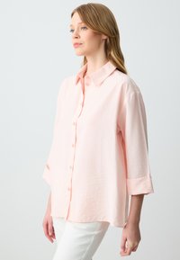 Camicia button-up rosa chiaro con colletto e maniche a tre quarti, caratterizzata da una vestibilità rilassata e un tessuto testurizzato.
