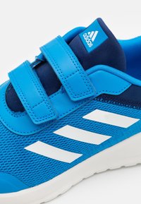 Chaussure de sport bleue en matériaux en maille et synthétiques, dotée de sangles Velcro, d'accents bleu marine et de trois rayures blanches sur le côté.