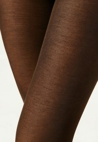 Collants marron côtelés avec une texture lisse, présentant une épaisseur moyenne et un éclat subtil, épousant étroitement les jambes sans motifs.