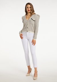 Beżowy kardigan w paski z poduszkami na ramionach, dekoltem w serek, zapięciem na guziki i czarnymi akcentami w postaci kieszeni, połączony z białymi jeansami skinny i cielistymi szpilkami.