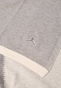 Κοντινή λήψη πλεκτού υφάσματος διπλωμένου με γκρι και λευκές ρίγες και μια μικρή κεντημένη σιλουέτα παίκτη μπάσκετ σε μέση άλματος.