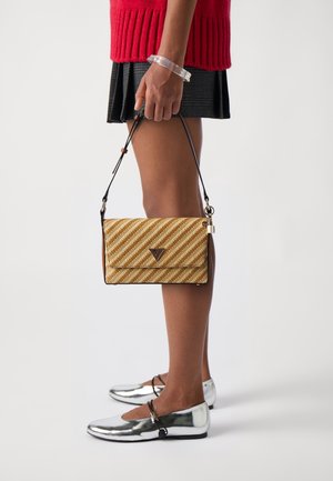 Personne portant des ballerines argentées, une jupe à carreaux noire, un pull rouge, tenant un petit sac à main beige rayé avec une bandoulière noire et un charm cadenas doré.