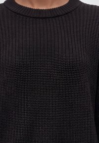 Gros plan d'une personne portant un pull en maille noire avec un col rond côtelé et une texture en point gaufré.