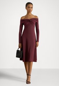 Bordo obleka brez ramen z dolgimi rokavi, oprijetim zgornjim delom in tekočo krilom. Kombinirana z majhno črno torbico in sandali z naramnicami.
