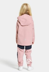 Rosa vattentät jacka med huva och elastiska ärmar, kombinerad med marinblå byxor med vita accenter och en logotyp. Vita sneakers fulländar looken.