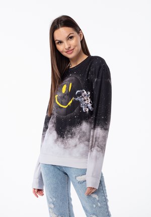 Black sweatshirt with galaxy print, featuring a large yellow smiley face and an astronaut graphic. Soft fabric, loose fit, and cuffed sleeves.