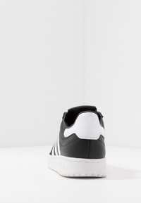 Svart lädersneaker med vita accenter, med tre horisontella ränder på sidan och en logotyp på hälkappan, gummisulor.