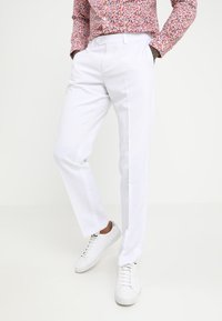 Pantalones blancos a medida de tela suave con corte recto, combinados con zapatillas blancas y una camisa rosa estampada.