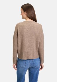 Bruine, zachte gebreide trui met een ronde hals en ribbelzoom. Heeft verlaagde schouders. Draagt met blauwe jeans. Gladde textuur.