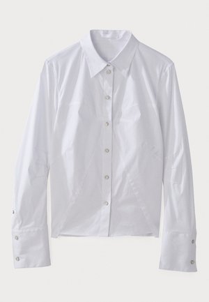 Camisa branca de manga longa feita de um tecido suave, com colarinho pontudo, botões frontais e costuras estruturadas para um ajuste ajustado. Acentos em botões prateados.