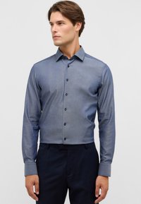 Slim-fit, langekleurige overhemden met lange mouwen in een gradient blauw stof. Voorzien van een puntige kraag, subtiele textuur en donkere knopen tegen een lichte achtergrond.