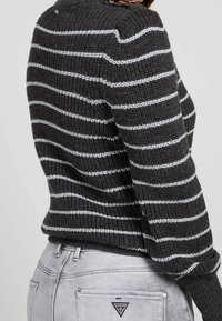 Gray striped knit sweater with white lines, featuring a textured fabric and loose fit, paired with light gray jeans displaying a logo patch.