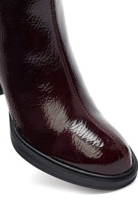 Stivaletto bordeaux con finitura lucida e testurizzata, punta rotonda, cuciture rosse a contrasto e suola in gomma nera.