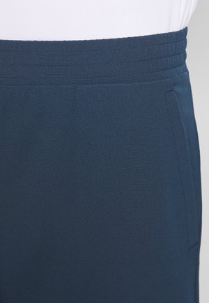 Zbliżenie na granatową spódnicę w pasie z przeszytym detalem paska i boczną kieszenią, noszoną z białą bluzką.