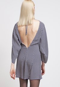 Šaty vzorované v námořnické modři a bílé barvě s hlubokým V výstřihem na zádech, tříčtvrtečními nafouklými rukávy a rozšířenou sukní. Lehká látka s hladkou texturou.