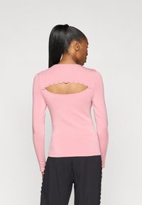 Pink long-sleeve top with a scalloped cutout at the back, made of soft fabric. Features a fitted design and a round neckline.