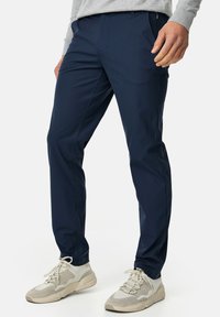 Navy trousers made of smooth fabric, featuring a slim fit design, side pockets, and a zipper closure. Paired with light sneakers.
