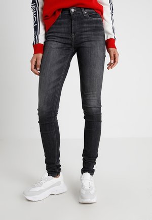 Modèle portant un jean slim gris foncé, un pull à rayures rouges et blanches et des baskets blanches, sur un fond de studio uni.