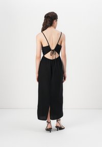 Robe maxi noire avec bretelles spaghetti ajustables, design dos nu et détail en cordon. Présente une fente avant et un tissu fluides et texturé.