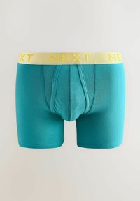 Türkiz boxer alsónadrág világos sárga derékrésszel, amelyen a "NEXT" márkajele látható. Az anyag simának és rugalmasnak tűnik, testhez simuló fazonnal.