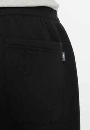 Close-up of black fabric pants with elastic waistband and back patch pocket featuring a small New Balance logo tag.