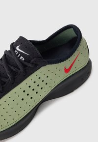 Must musta ja oliivroheline Nike spordijalanõud, millel on perforatsiooniga külgpaneelid, mustad paelad, punane tikandiga swoosh ja must tallal valge taust.