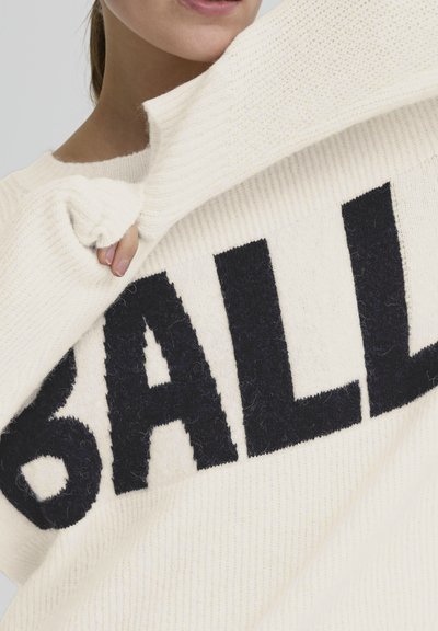 Pull crème avec un tricot texturé et un audacieux graphisme noir "BALL" sur le devant. Le tissu semble doux et légèrement duveteux.