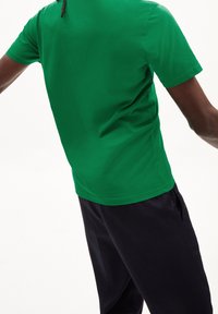 Zelené tričko s krátkým rukávem z bavlny, s kulatým výstřihem a volným střihem, spárováno s tmavě modrými kalhotami.