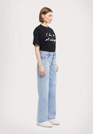Svart bomull t-skjorte med hvit håndskrevet tekst, kombinert med lyseblå høyt midje vide denimjeans og hvite sko.
