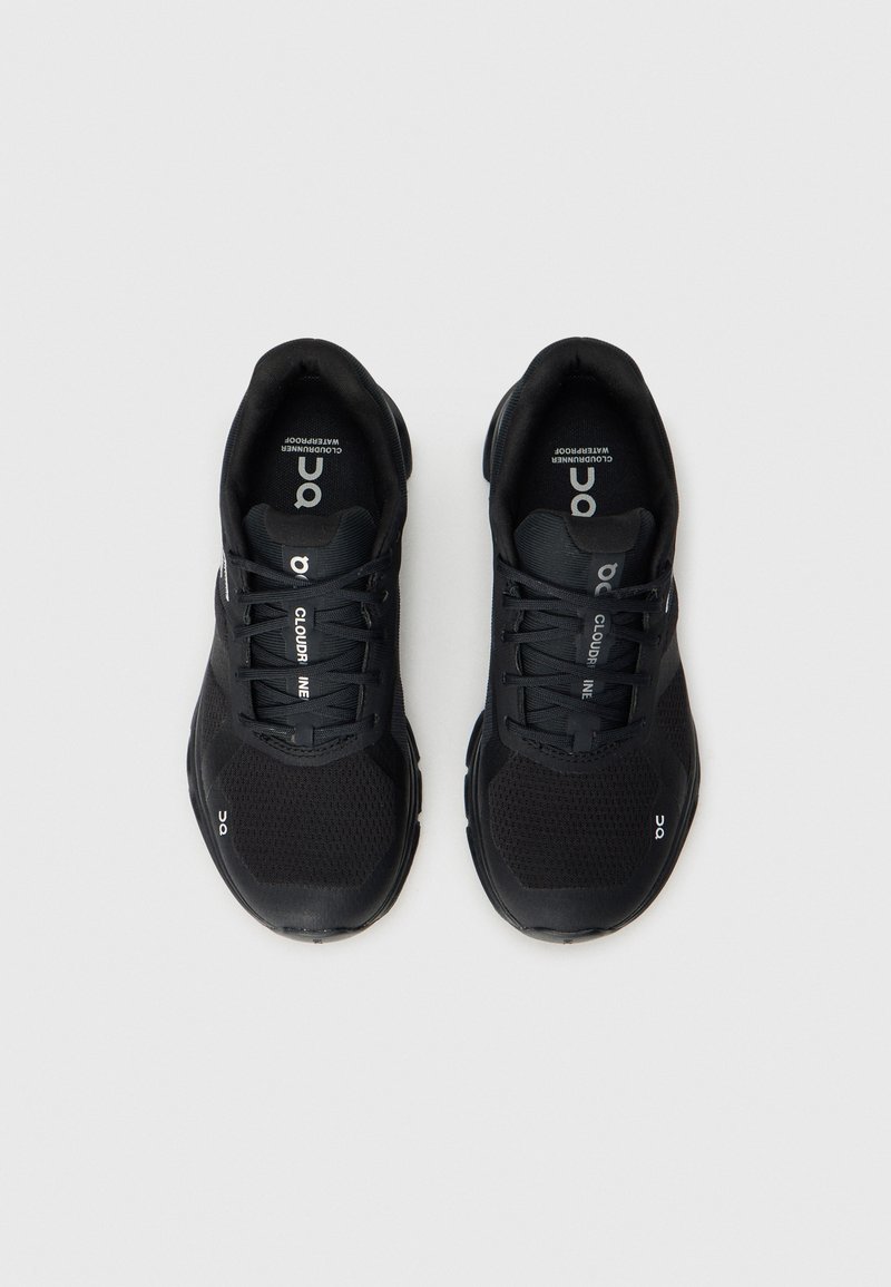 Zapatillas deportivas negras con parte superior de malla y sintético, que presentan una puntera redondeada, cierre de cordones y acentos reflectantes. Diseño de suela ligera.