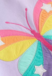 Šareni vezeni leptir na ljubičastoj pozadini, s krilima u bojama duge, ružičastim naglascima i bijelim detaljima u obliku zvijezda. Mekana tekstura tkanine.