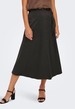 Woman wearing a black midi wrap skirt with tie detail, paired with black heeled sandals and a brown sleeveless top.