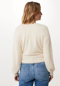 Cremefarbenes, flauschiges Sweatshirt mit langen Ärmeln und einem taillierten Bund, kombiniert mit blauen Jeans aus Denim mit klassischen Gesäßtaschen.
