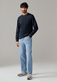 Maglietta nera a maniche lunghe abbinata a jeans azzurri chiari e sneakers grigie. Stile casual, materiale in cotone e maniche risvoltabili.