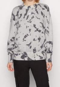 Sudadera gris con patrón tie-dye negro, cuello redondo, mangas largas y un pequeño logo blanco de Nike en el pecho. Cuenta con puños y dobladillo elásticos.