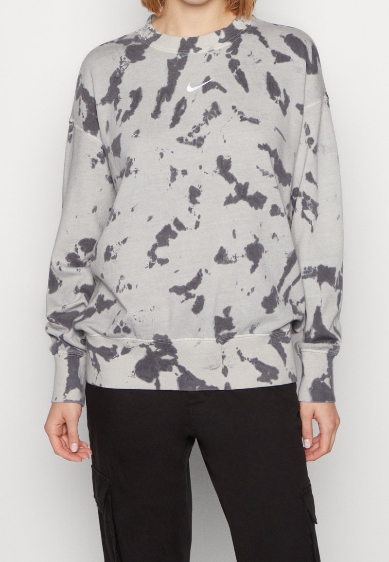 Sudadera gris con patrón tie-dye negro, cuello redondo, mangas largas y un pequeño logo blanco de Nike en el pecho. Cuenta con puños y dobladillo elásticos.