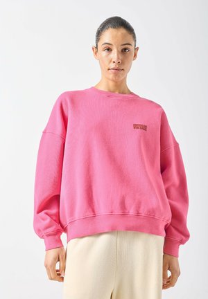 Pink sweatshirt with a round neck, dropped shoulders, and ribbed cuffs. Features small “American Vintage” logo on the chest. Soft texture.