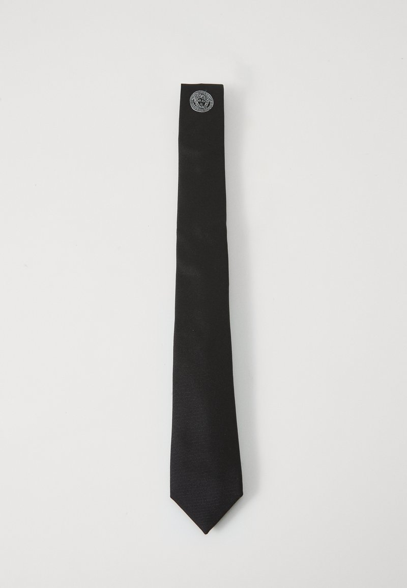 Cravate en satin noir avec une texture lisse, comportant un emblème logo en argent à l'extrémité étroite. Conçue avec une forme classique et élancée.